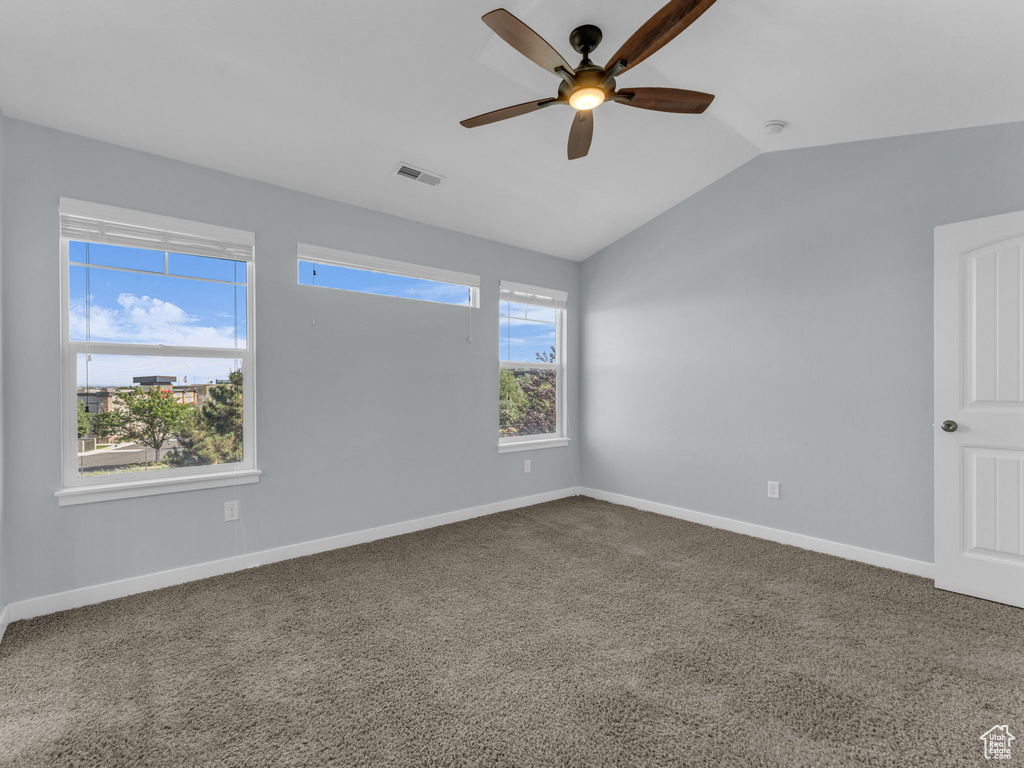 Carpeted empty room featuring ceiling fan, vaulted ceiling, and a smoke detector