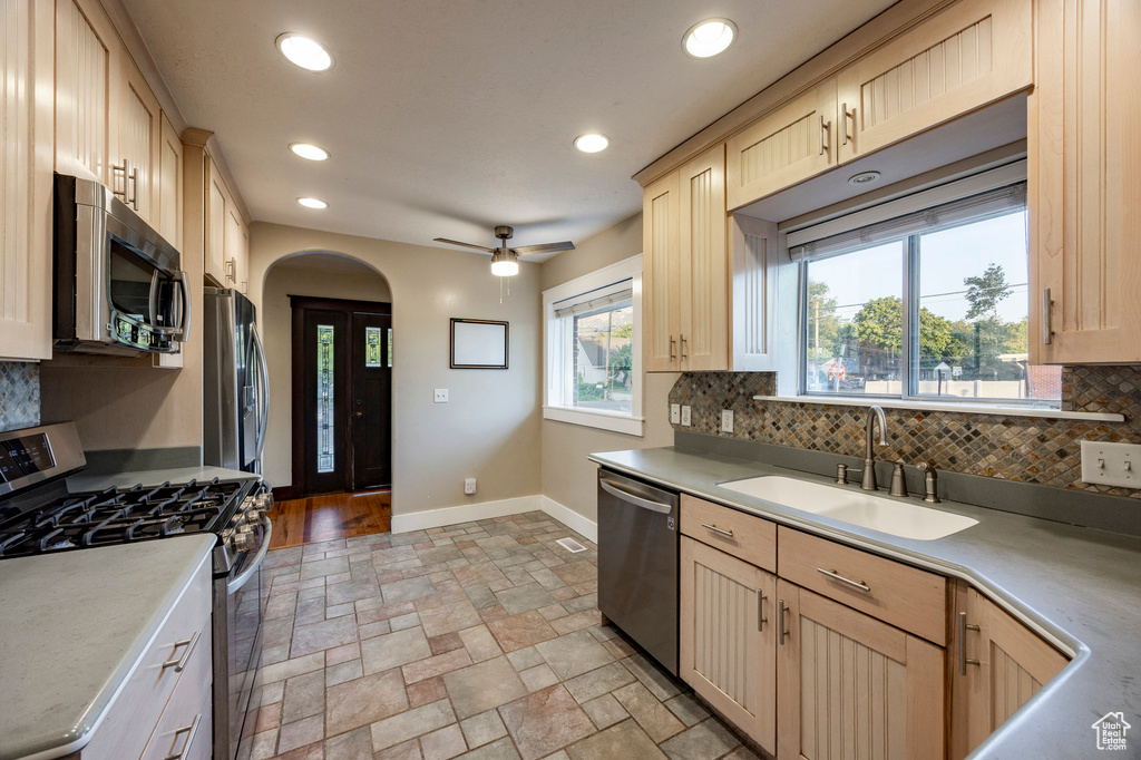 Kitchen with appliances with stainless steel finishes, light brown cabinets, arched walkways, decorative backsplash, and recessed lighting