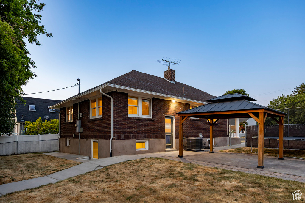 Back of house with a gazebo, brick siding, a patio area, and a chimney