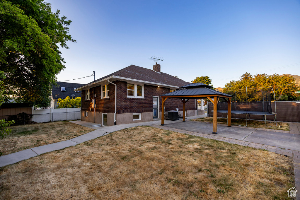 Rear view of property featuring a trampoline, a gazebo, brick siding, a patio, and a fenced backyard