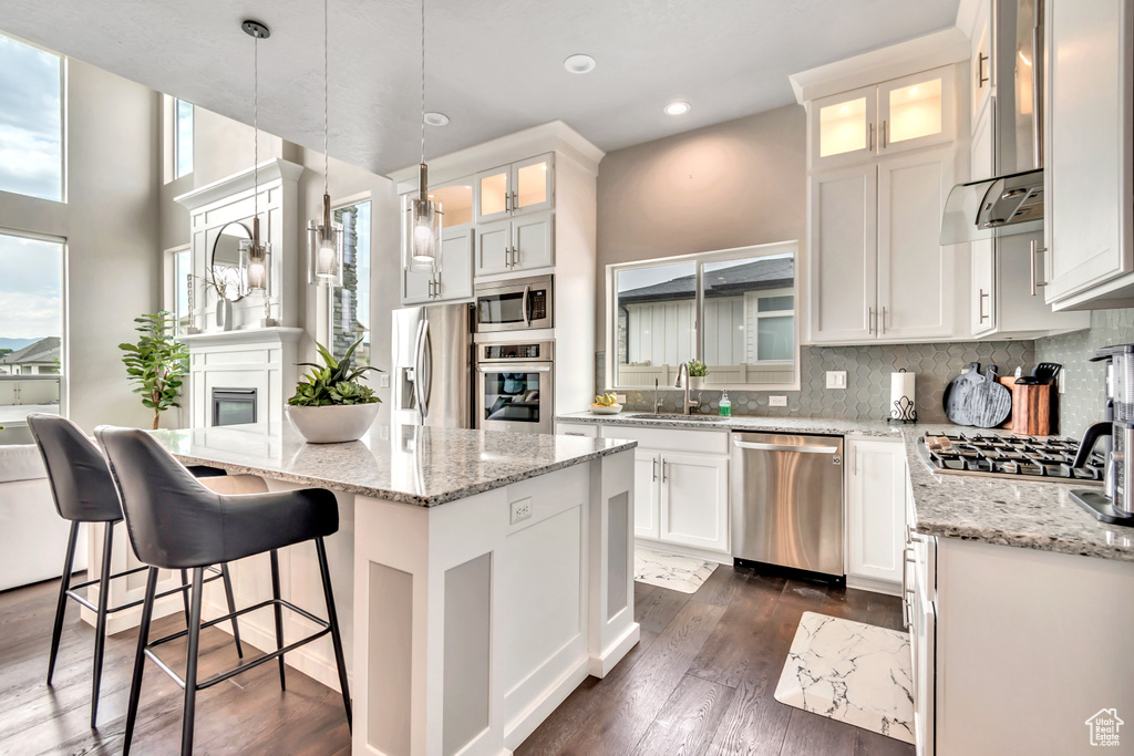 Kitchen with appliances with stainless steel finishes, wall chimney range hood, a kitchen island, decorative backsplash, and white cabinets