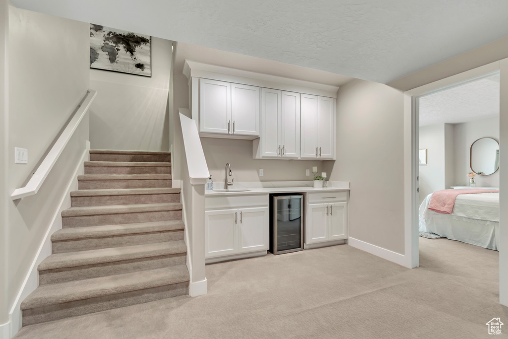 Indoor wet bar featuring beverage cooler, light carpet, and stairs