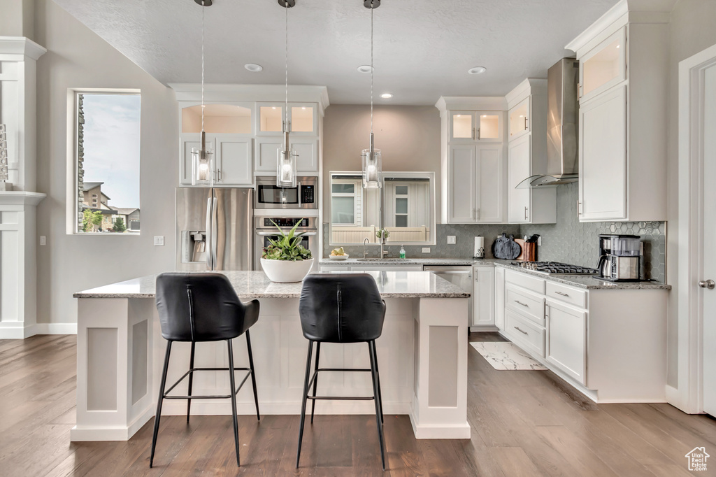 Kitchen with wall chimney exhaust hood, stainless steel appliances, a kitchen island, decorative backsplash, and white cabinets
