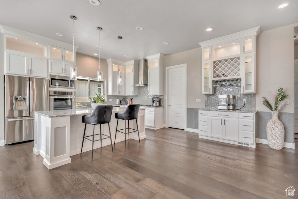 Kitchen featuring stainless steel appliances, wall chimney range hood, white cabinetry, and recessed lighting