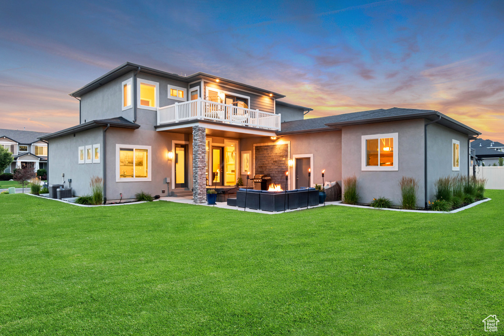 Back of property at dusk featuring a balcony, stucco siding, a yard, and a patio area