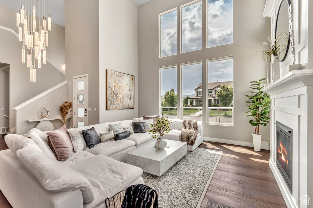 Living area featuring a towering ceiling, a glass covered fireplace, wood finished floors, and a chandelier