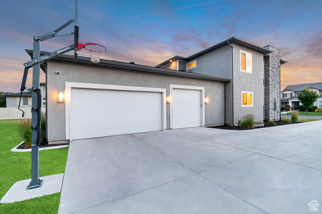 Property exterior at dusk with a garage, concrete driveway, stucco siding, and a yard