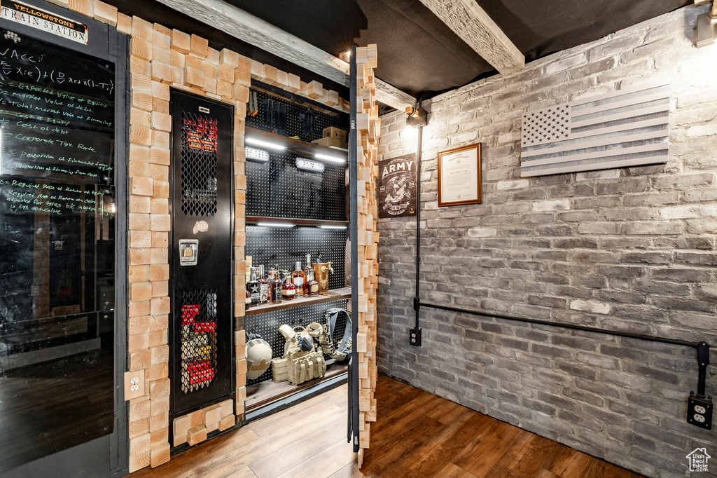 Wine room with wood finished floors, beam ceiling, and brick wall