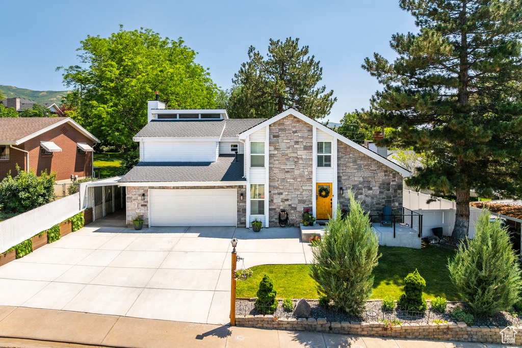Mid-century inspired home featuring stone siding, driveway, a chimney, and roof with shingles