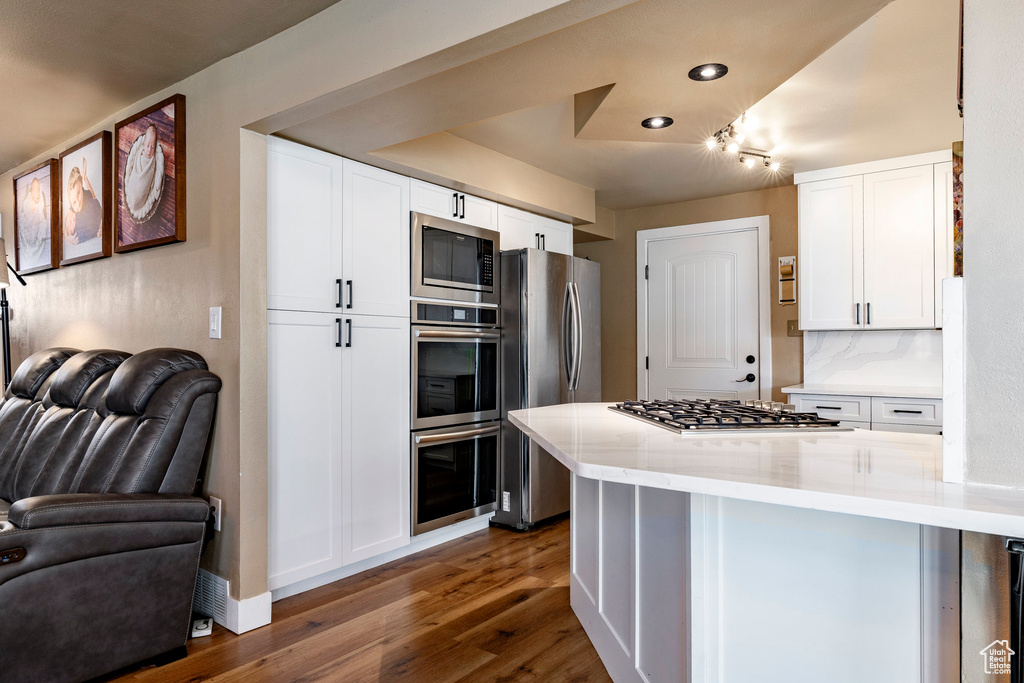 Kitchen with appliances with stainless steel finishes, open floor plan, dark wood finished floors, white cabinetry, and recessed lighting