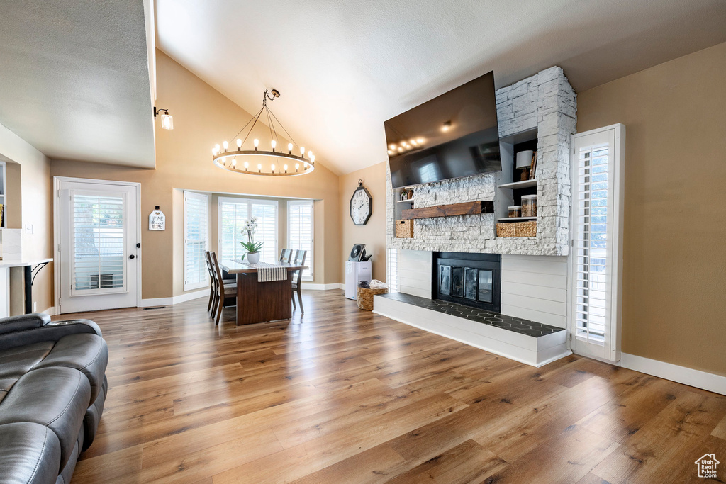 Living area with a chandelier, wood finished floors, built in features, a stone fireplace, and high vaulted ceiling
