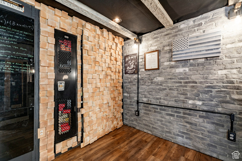 Wine area featuring brick wall, beam ceiling, and wood finished floors