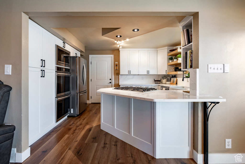 Kitchen featuring appliances with stainless steel finishes, open shelves, a peninsula, dark wood-style floors, and white cabinetry