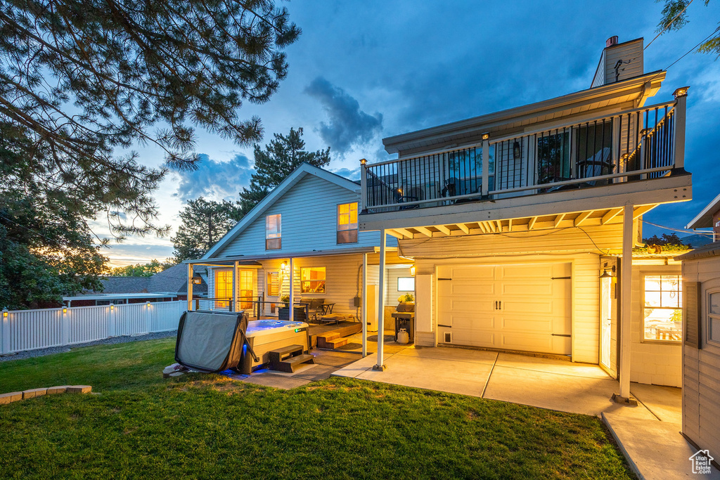 Back of property at dusk with a balcony, an attached garage, and a patio