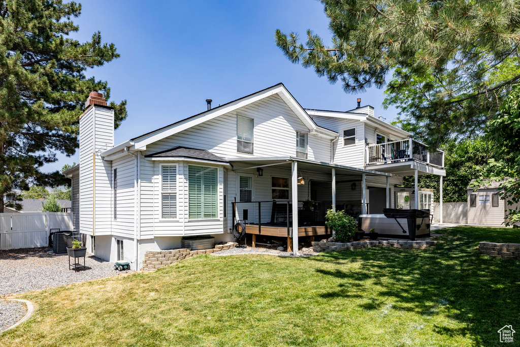 Back of property with a chimney, a hot tub, and a deck