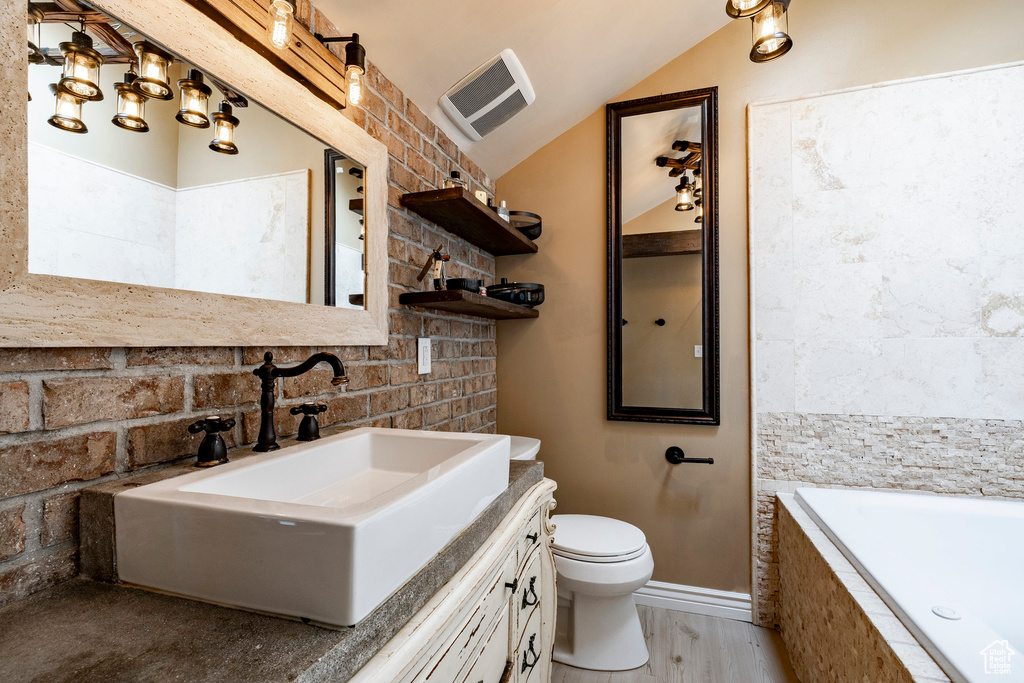 Bathroom featuring tiled tub, vaulted ceiling, vanity, wood finished floors, and decorative backsplash