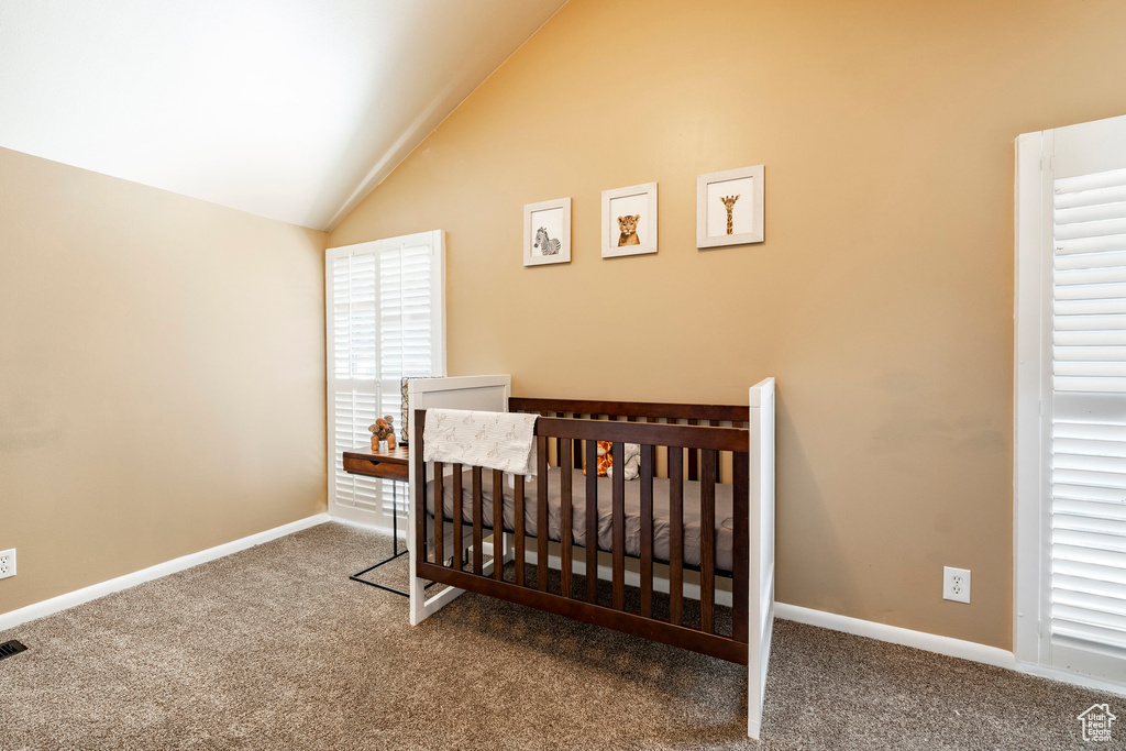 Carpeted bedroom featuring vaulted ceiling and a crib