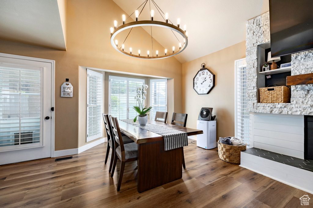 Dining area with a chandelier, wood finished floors, high vaulted ceiling, and a fireplace