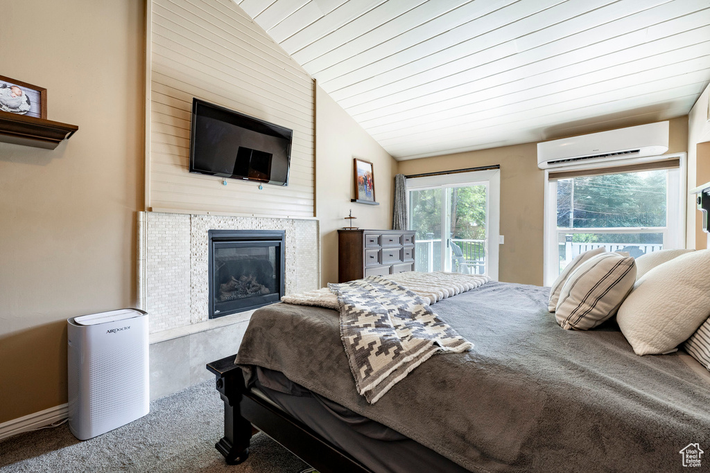 Bedroom with an AC wall unit, carpet flooring, access to outside, a fireplace, and vaulted ceiling
