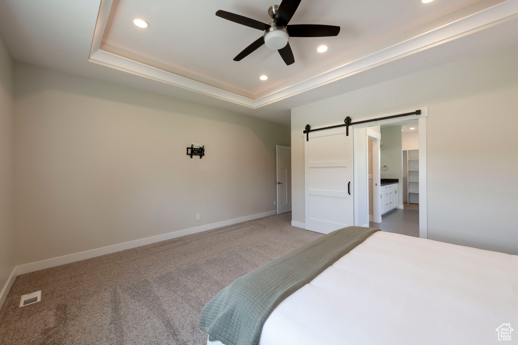 Bedroom featuring a barn door, recessed lighting, a raised ceiling, light colored carpet, and a spacious closet