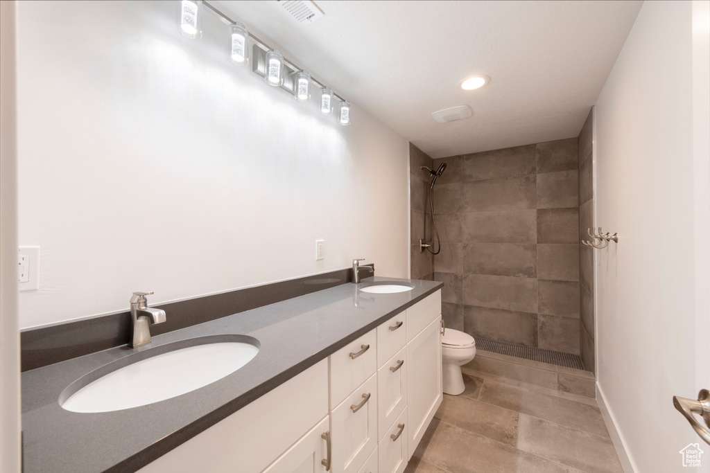 Bathroom featuring a tile shower, double vanity, and recessed lighting