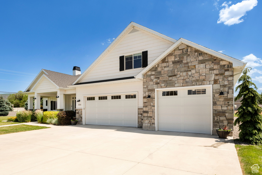 View of front of property with driveway, stone siding, a chimney, and an attached garage