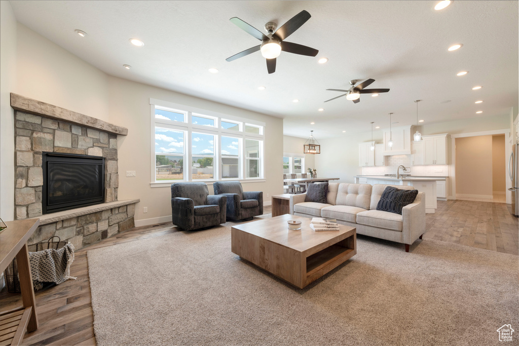 Living room with a ceiling fan, recessed lighting, light wood-type flooring, and a stone fireplace