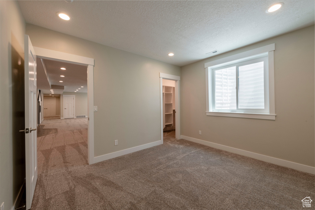 Unfurnished bedroom with light colored carpet, recessed lighting, a spacious closet, and a textured ceiling