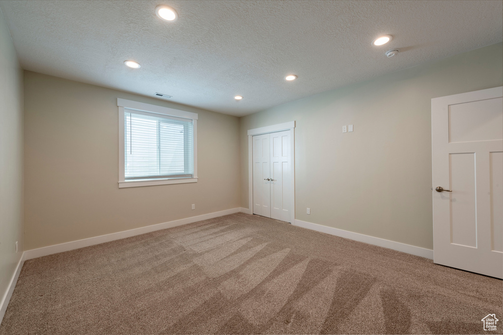 Unfurnished bedroom featuring light carpet, recessed lighting, a closet, and a textured ceiling