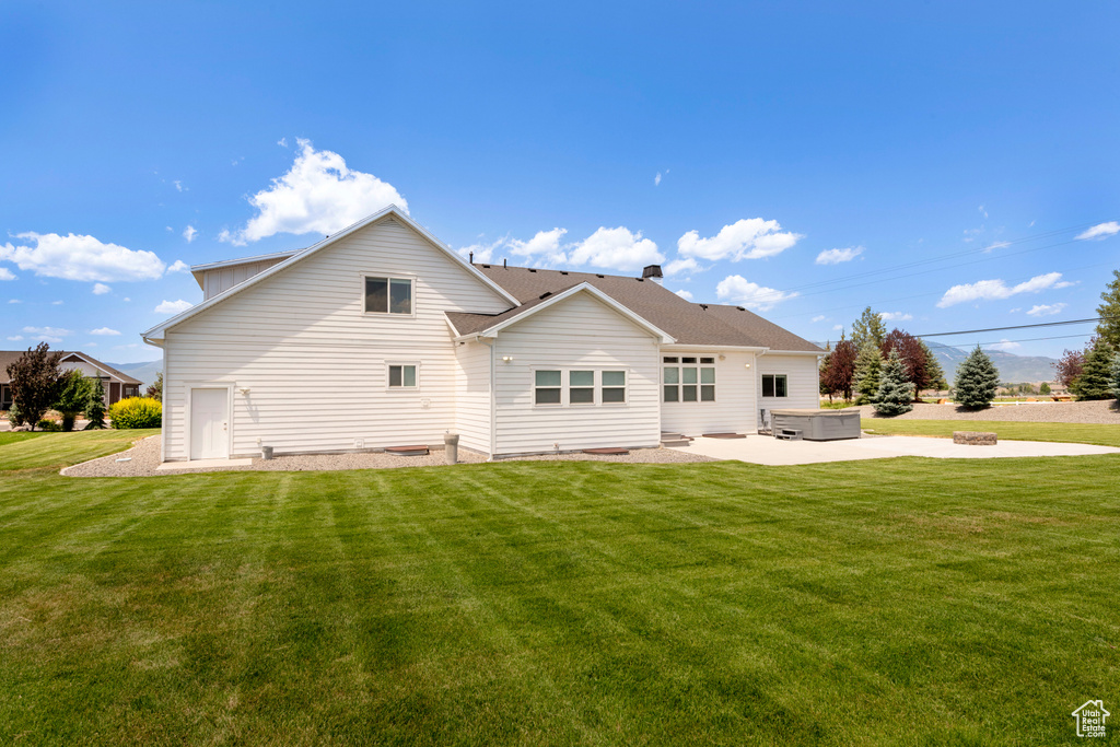 Back of house featuring a hot tub, a lawn, and a patio