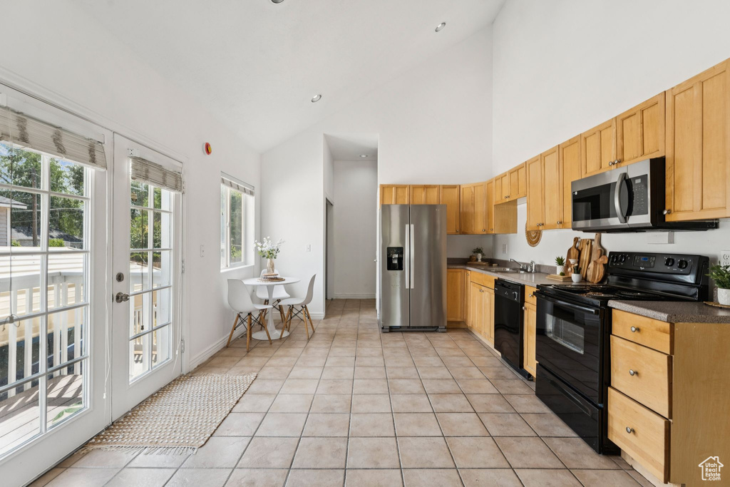 Kitchen with black appliances, high vaulted ceiling, light tile patterned flooring, dark countertops, and light brown cabinetry