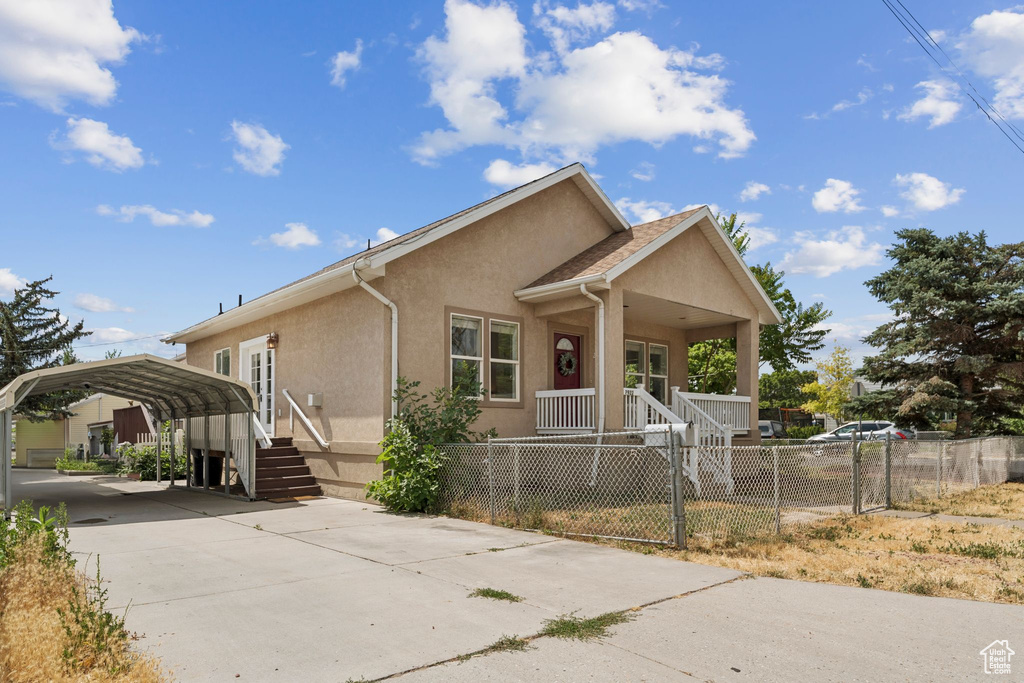 View of front facade featuring covered porch, a carport, a fenced front yard, stucco siding, and driveway