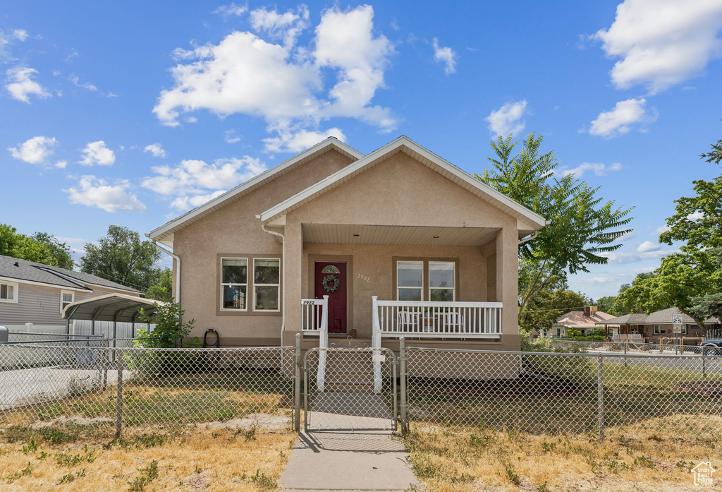 Bungalow-style house with covered porch, a fenced front yard, a gate, a carport, and stucco siding