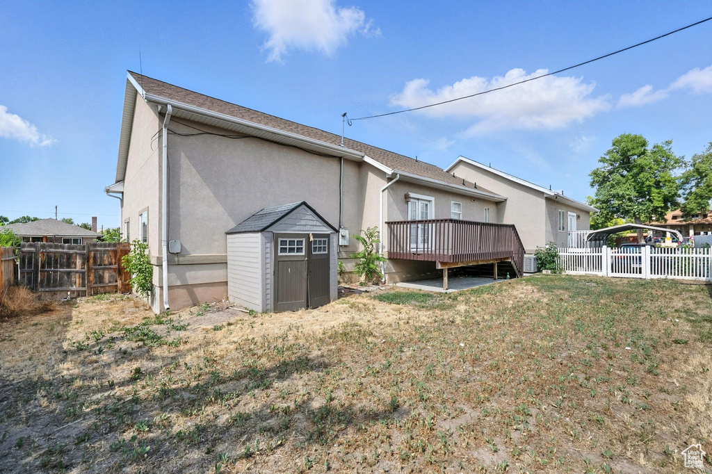 Rear view of house with a deck, a storage unit, a fenced backyard, and stucco siding