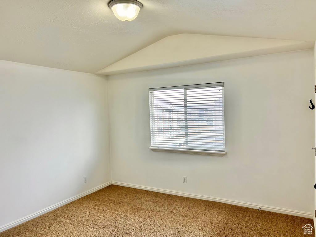 Carpeted empty room featuring vaulted ceiling and a textured ceiling