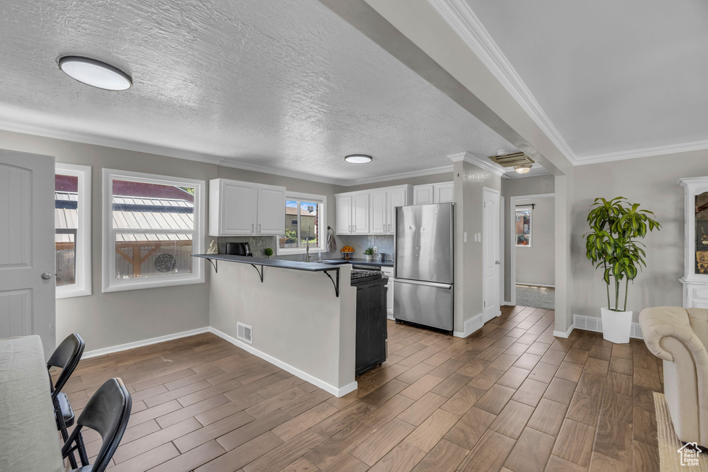 Kitchen with freestanding refrigerator, dark countertops, a peninsula, white cabinetry, and a kitchen bar