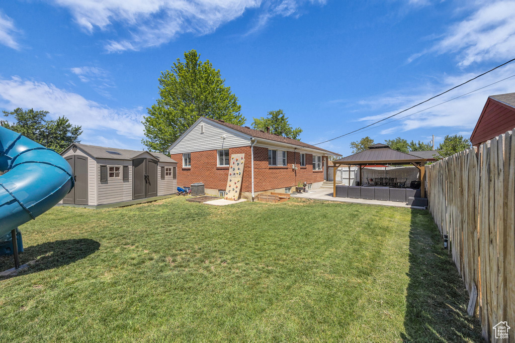 Rear view of property featuring a gazebo, brick siding, a shed, a fenced backyard, and a patio