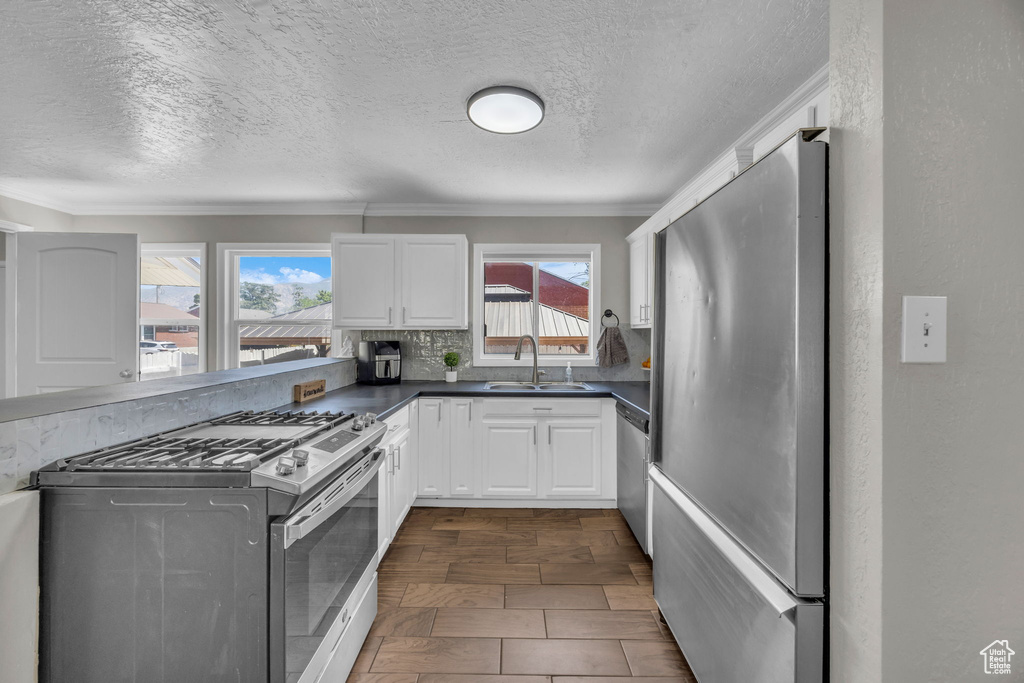 Kitchen with stainless steel appliances, dark countertops, a textured ceiling, white cabinets, and tasteful backsplash