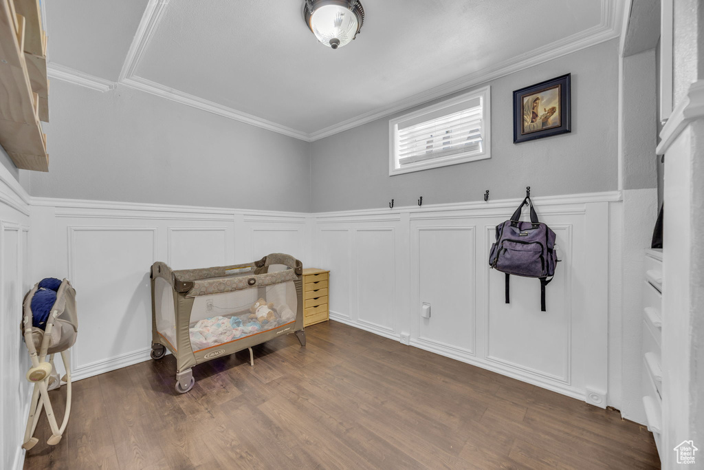 Bedroom with a decorative wall, dark wood finished floors, a wainscoted wall, and ornamental molding