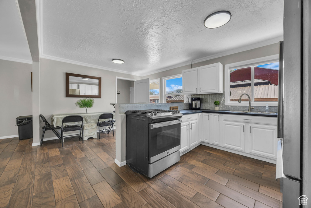 Kitchen with stainless steel appliances, white cabinets, dark wood-style floors, dark countertops, and crown molding