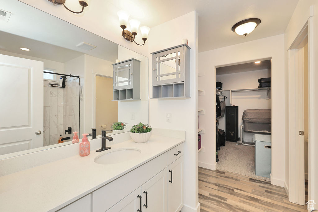 Bathroom with a spacious closet, vanity, tiled shower, and wood finished floors