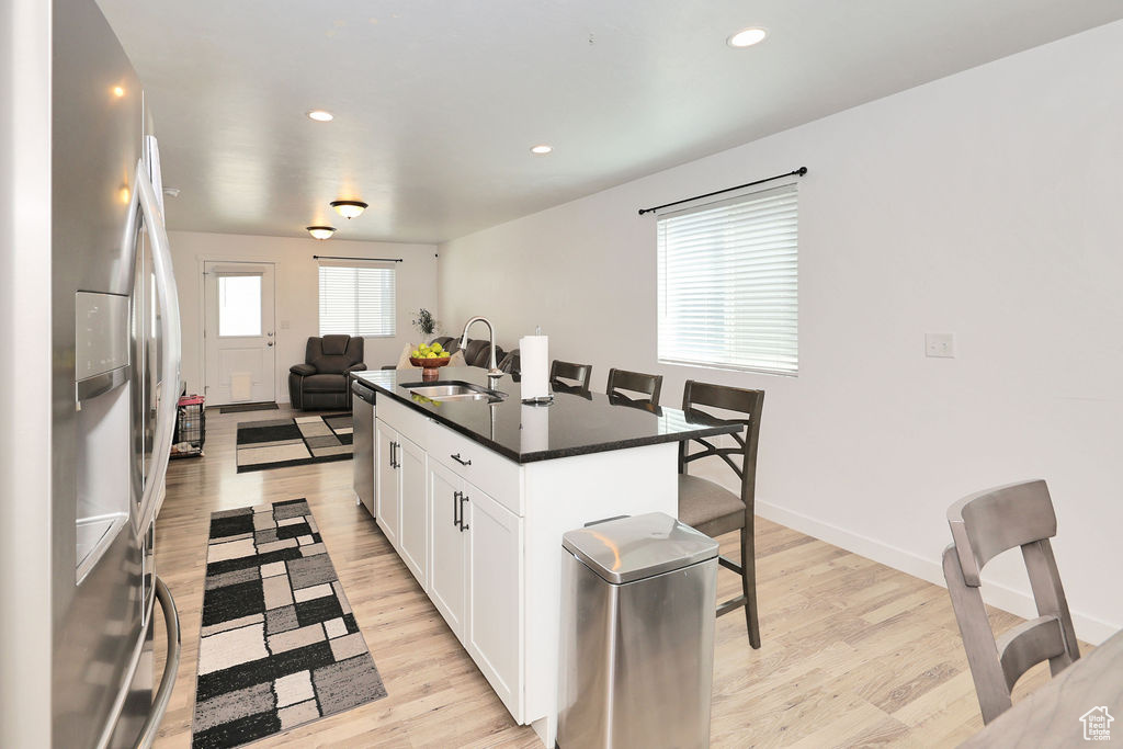 Kitchen with appliances with stainless steel finishes, dark countertops, open floor plan, white cabinetry, and an island with sink