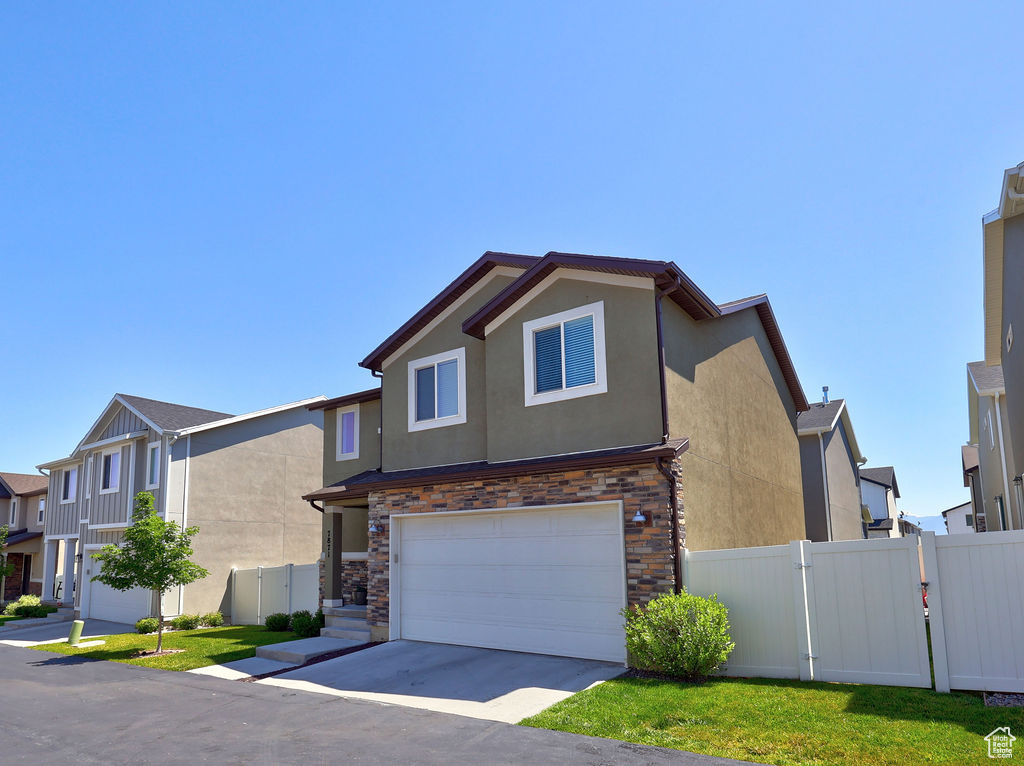 View of front of home with stucco siding, an attached garage, driveway, stone siding, and a gate