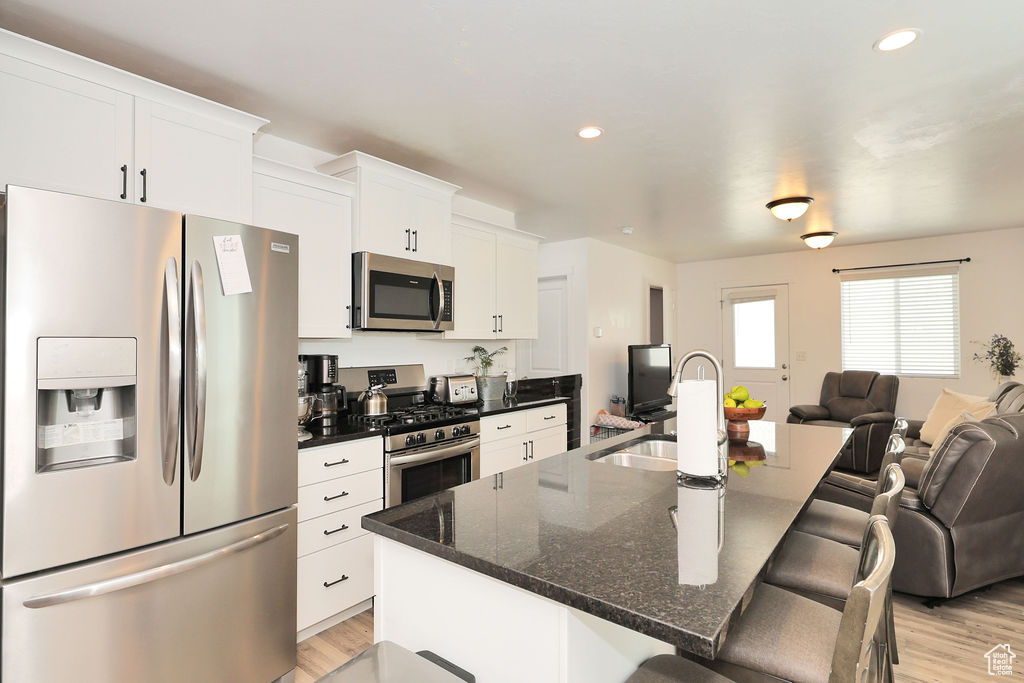 Kitchen featuring appliances with stainless steel finishes, open floor plan, light wood-type flooring, a breakfast bar, and white cabinets