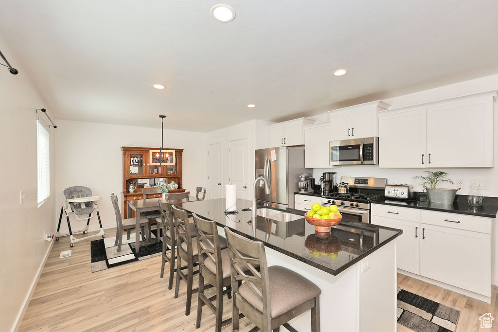 Kitchen with appliances with stainless steel finishes, light wood-type flooring, a breakfast bar, white cabinetry, and an island with sink