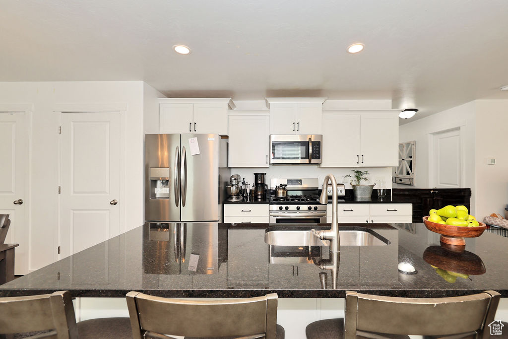 Kitchen with appliances with stainless steel finishes, a kitchen bar, white cabinetry, a large island with sink, and recessed lighting