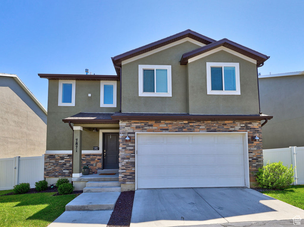 View of front of house with stucco siding, stone siding, concrete driveway, and an attached garage
