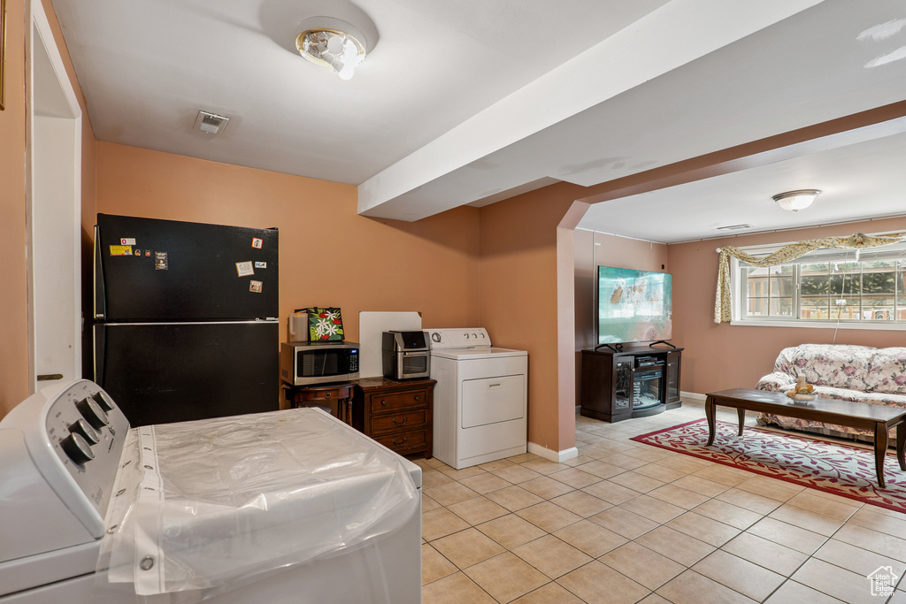 Kitchen featuring freestanding refrigerator, stainless steel microwave, washer / clothes dryer, and light tile patterned flooring