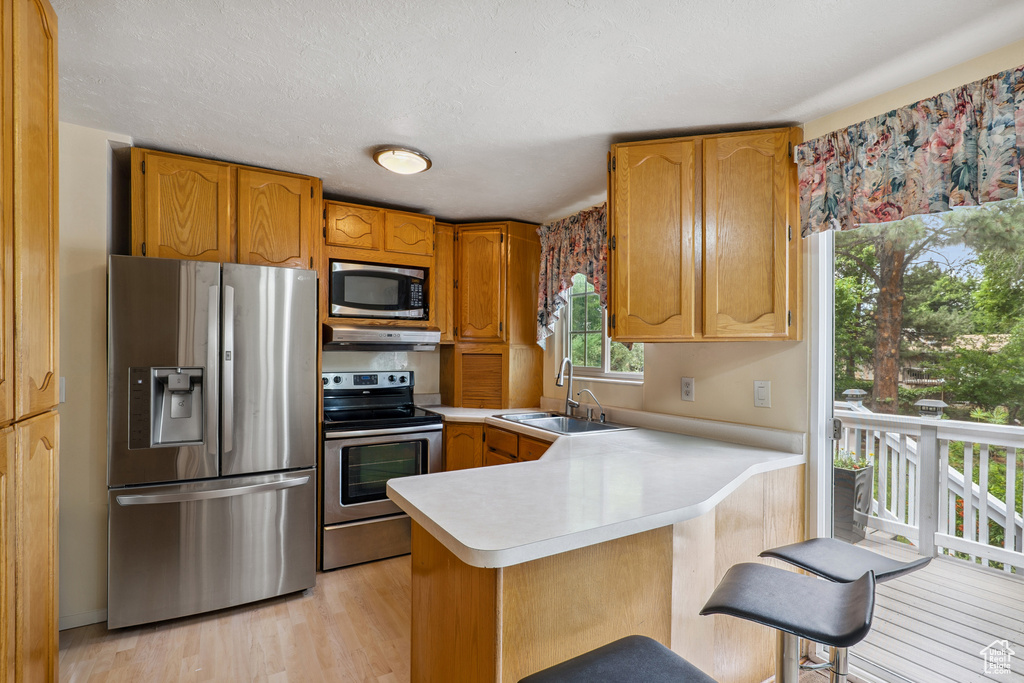 Kitchen with stainless steel appliances, light countertops, a peninsula, light wood-type flooring, and under cabinet range hood