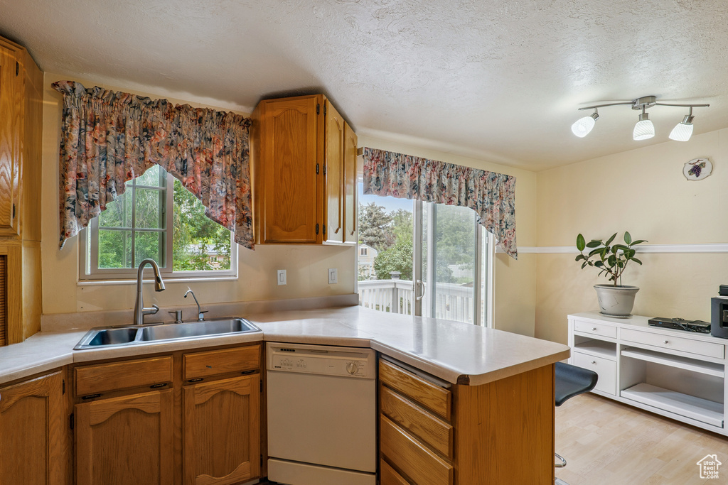 Kitchen featuring dishwasher, a peninsula, light countertops, a textured ceiling, and brown cabinets